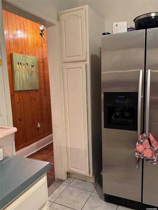 kitchen with wood walls, light tile patterned floors, and stainless steel refrigerator with ice dispenser