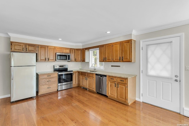 kitchen with ornamental molding, sink, appliances with stainless steel finishes, and light hardwood / wood-style flooring