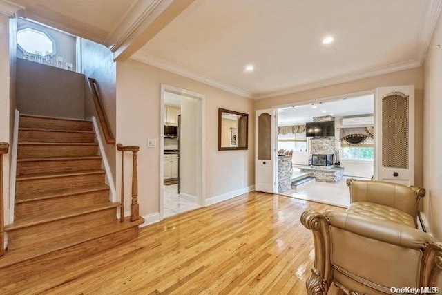 living room with a wall unit AC, a stone fireplace, crown molding, and light wood-type flooring