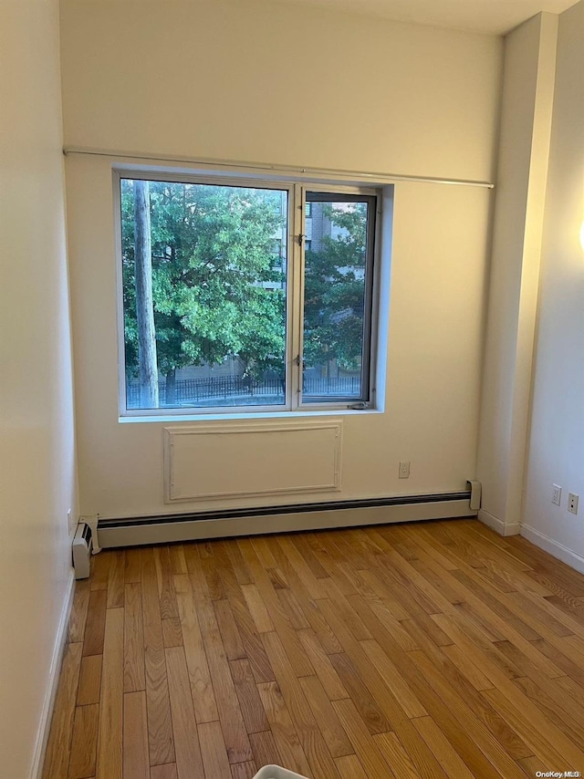 unfurnished room with a wealth of natural light, a baseboard heating unit, and light wood-type flooring