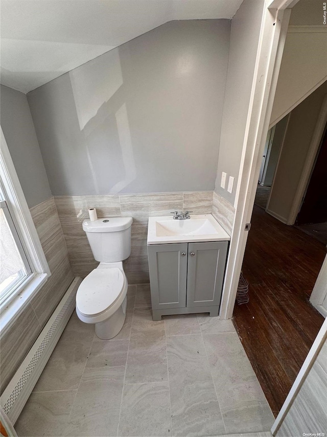 bathroom featuring vanity, a baseboard heating unit, tile walls, hardwood / wood-style floors, and lofted ceiling