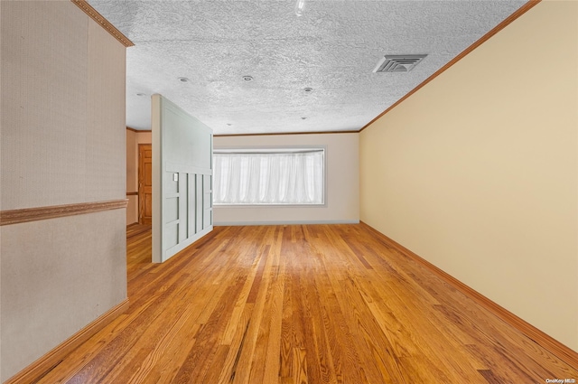 empty room with a textured ceiling, light hardwood / wood-style floors, and crown molding