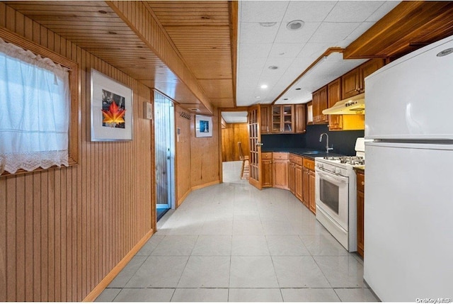 kitchen featuring light tile patterned flooring, white appliances, wooden ceiling, and wood walls