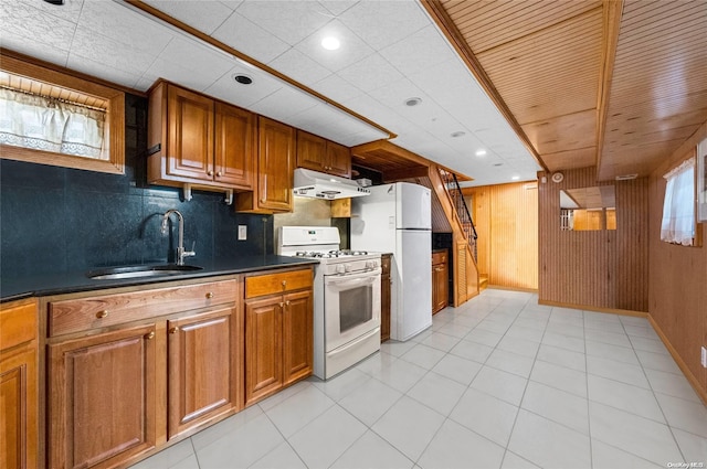 kitchen featuring backsplash, white appliances, sink, and wooden walls