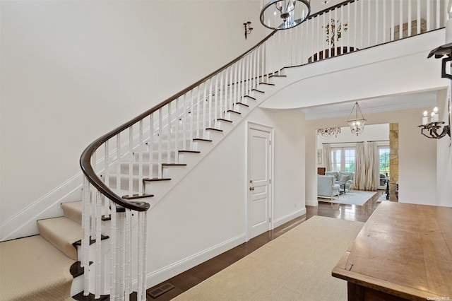 stairway with crown molding, french doors, wood-type flooring, and an inviting chandelier