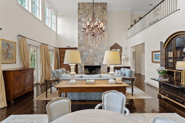 living room featuring crown molding, a stone fireplace, a towering ceiling, and dark wood-type flooring