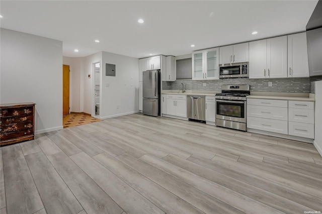 kitchen with white cabinets, light wood-type flooring, appliances with stainless steel finishes, and tasteful backsplash