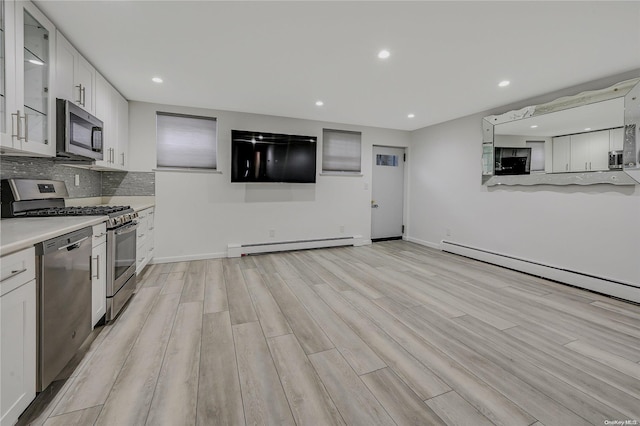 kitchen with appliances with stainless steel finishes, light wood-type flooring, backsplash, baseboard heating, and white cabinets