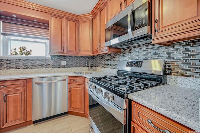 kitchen with backsplash, light stone counters, sink, and appliances with stainless steel finishes