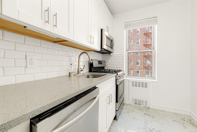 kitchen with radiator, light stone countertops, sink, stainless steel appliances, and white cabinets