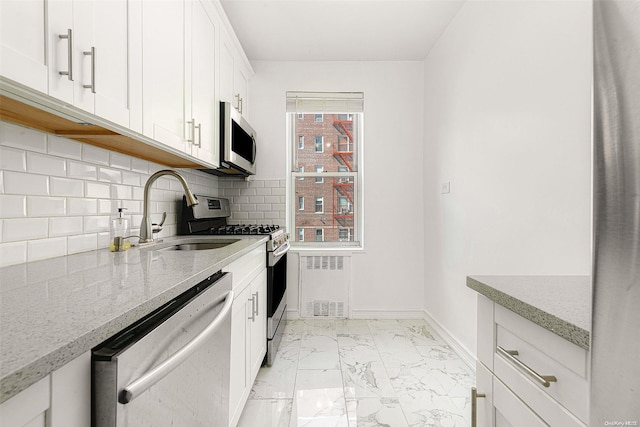 kitchen featuring light stone counters, radiator, stainless steel appliances, sink, and white cabinets