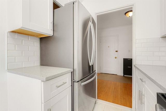 kitchen with light stone countertops, stainless steel fridge, white cabinetry, and light hardwood / wood-style flooring