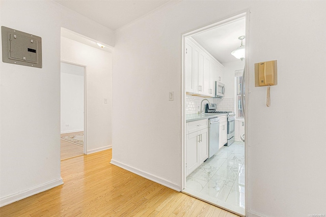 kitchen featuring electric panel, decorative backsplash, light wood-type flooring, white cabinetry, and stainless steel appliances