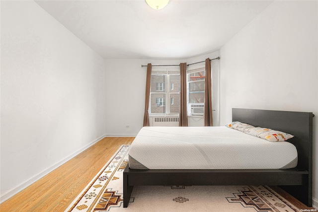 bedroom with radiator heating unit, cooling unit, and hardwood / wood-style flooring