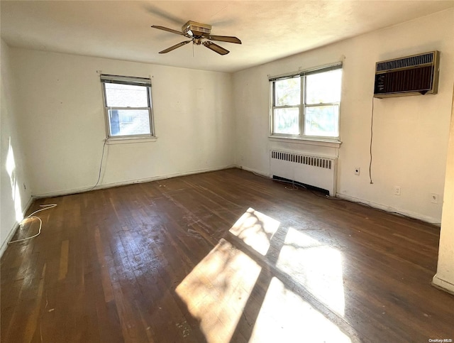 empty room featuring a healthy amount of sunlight, radiator, a wall mounted AC, and hardwood / wood-style flooring