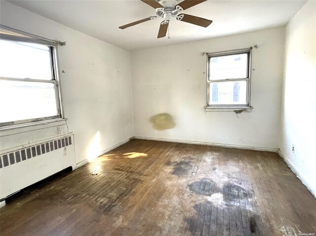 unfurnished room featuring hardwood / wood-style flooring, radiator heating unit, and plenty of natural light