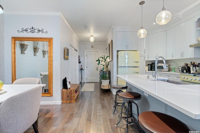 kitchen featuring light wood-type flooring, decorative light fixtures, a kitchen bar, white cabinets, and ornamental molding