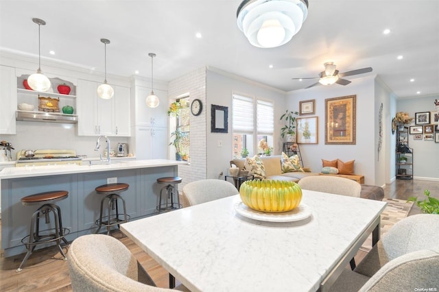 dining space featuring light wood-type flooring, ceiling fan, crown molding, and sink