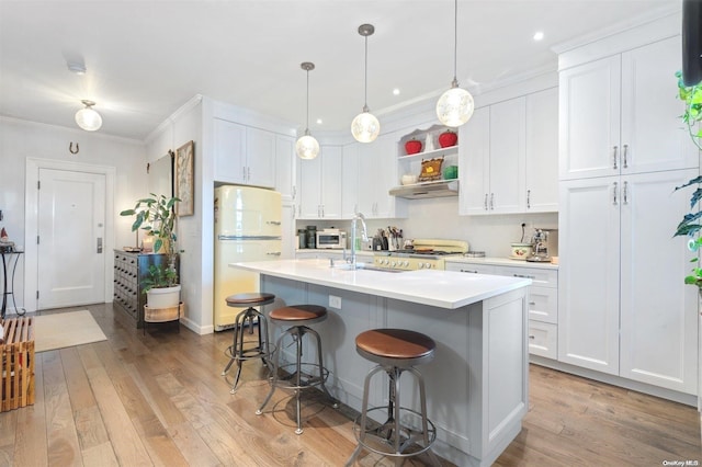 kitchen featuring light wood-type flooring, white refrigerator, a center island with sink, and white cabinetry