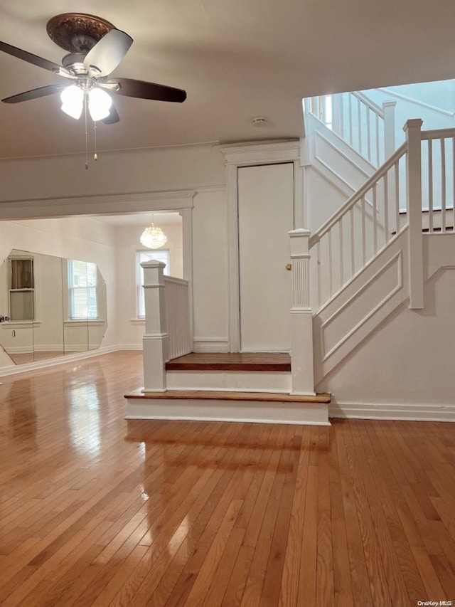 staircase with hardwood / wood-style floors and ceiling fan with notable chandelier