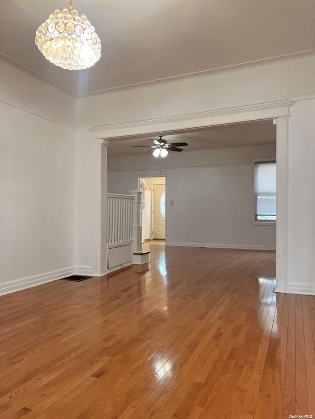 empty room featuring ceiling fan with notable chandelier and hardwood / wood-style flooring