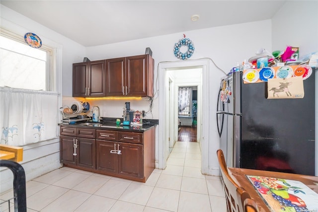 kitchen with black refrigerator, dark brown cabinetry, sink, radiator heating unit, and light tile patterned flooring