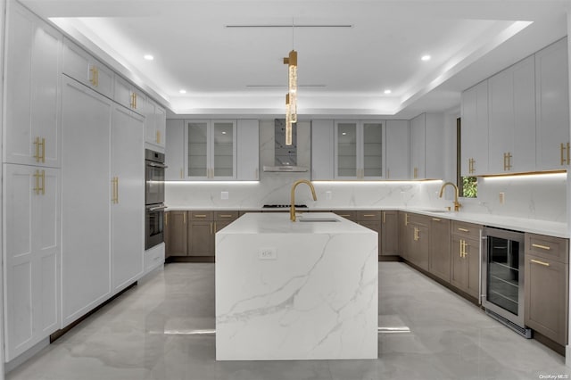 kitchen featuring decorative light fixtures, a tray ceiling, a kitchen island with sink, and beverage cooler