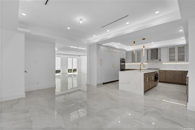 kitchen featuring pendant lighting, wall chimney exhaust hood, light stone counters, and a tray ceiling