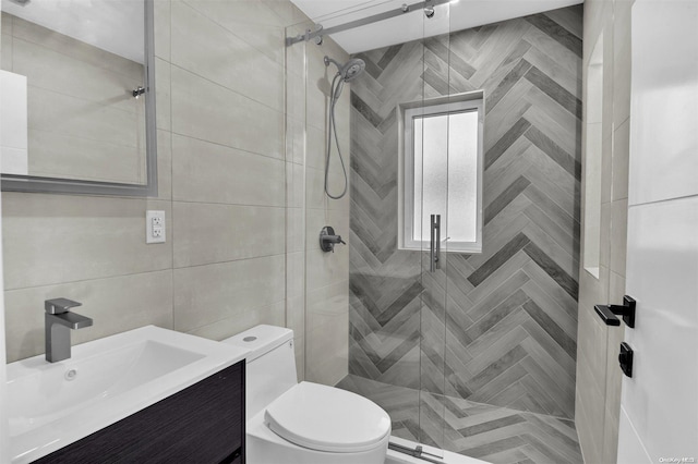 bathroom with a tile shower, vanity, tile walls, and toilet