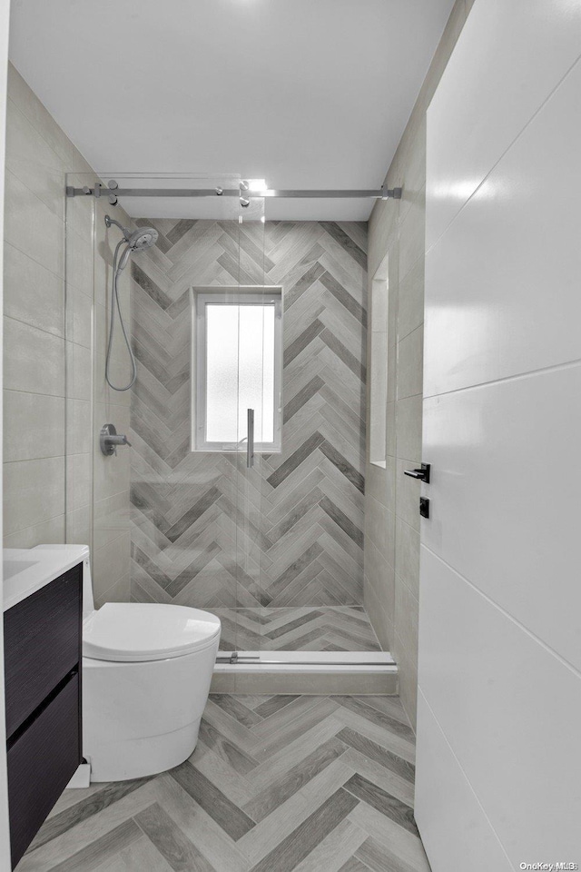 bathroom featuring a shower with door, vanity, tile walls, and toilet