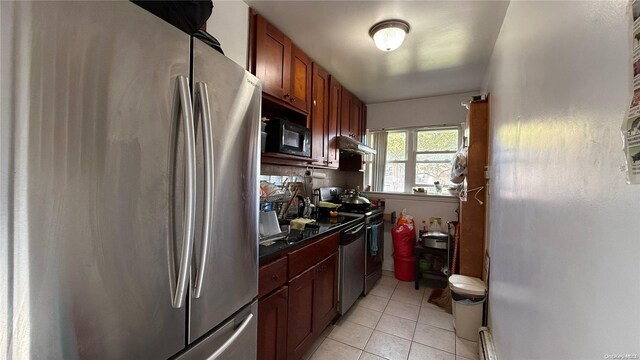 kitchen with light tile patterned floors, under cabinet range hood, stainless steel appliances, brown cabinetry, and dark countertops