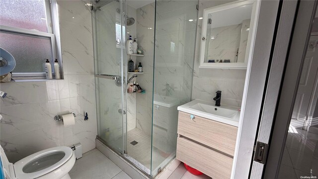 full bath featuring toilet, a marble finish shower, tile walls, and vanity