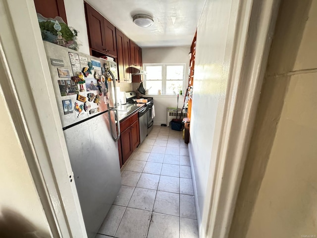 kitchen featuring under cabinet range hood, light tile patterned flooring, range, and freestanding refrigerator