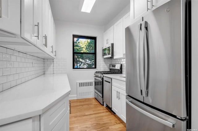 kitchen with tasteful backsplash, white cabinets, stainless steel appliances, and light wood-type flooring