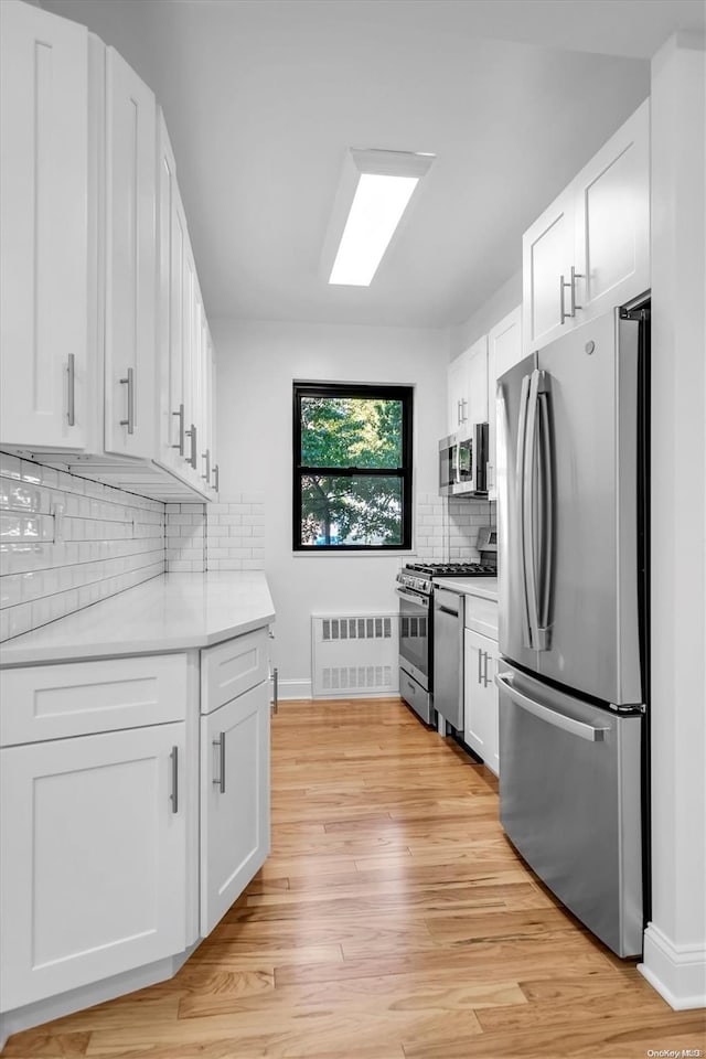 kitchen featuring white cabinets, light wood-type flooring, stainless steel appliances, and tasteful backsplash