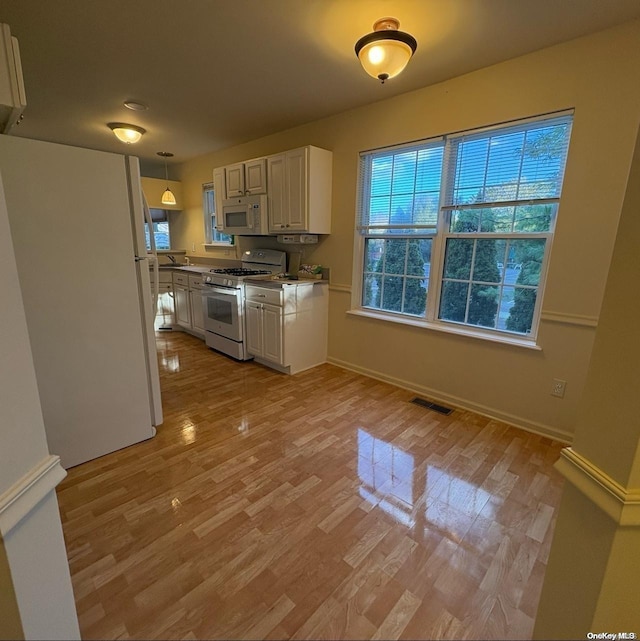 kitchen with white appliances, plenty of natural light, decorative light fixtures, and white cabinets