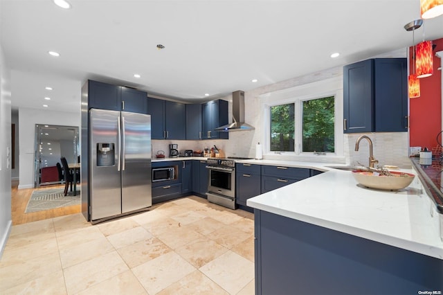 kitchen featuring blue cabinetry, hanging light fixtures, stainless steel appliances, and wall chimney range hood