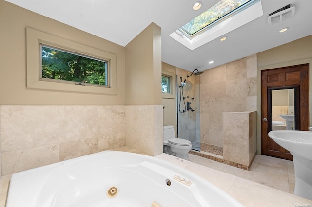 bathroom with plus walk in shower, a skylight, tile patterned flooring, toilet, and tile walls