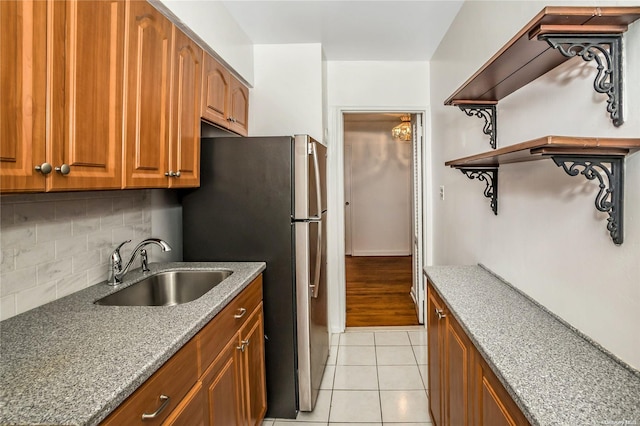 kitchen featuring sink, decorative backsplash, light stone countertops, light tile patterned floors, and stainless steel refrigerator