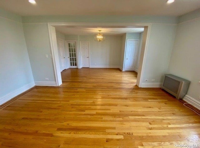 unfurnished room with radiator heating unit, light wood-type flooring, and a notable chandelier