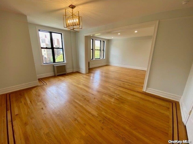 unfurnished room with a chandelier, radiator heating unit, and light hardwood / wood-style flooring