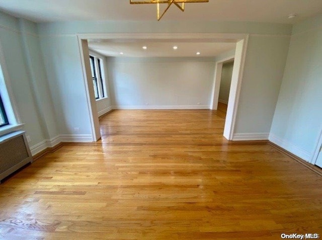 spare room featuring a chandelier, radiator heating unit, and light hardwood / wood-style flooring