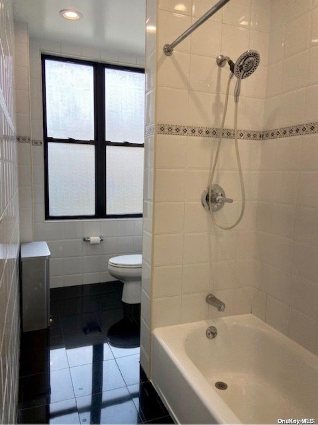 bathroom with tile patterned floors, tiled shower / bath, tile walls, and toilet