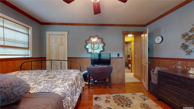 bedroom with ceiling fan, light hardwood / wood-style flooring, wooden walls, a closet, and ornamental molding