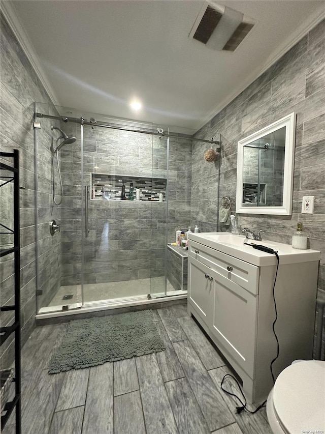 bathroom with toilet, vanity, a shower with shower door, tile walls, and ornamental molding