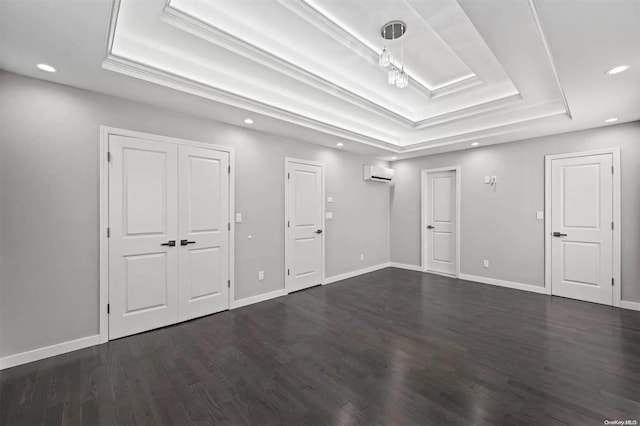 spare room featuring a raised ceiling, dark hardwood / wood-style flooring, crown molding, and a wall unit AC