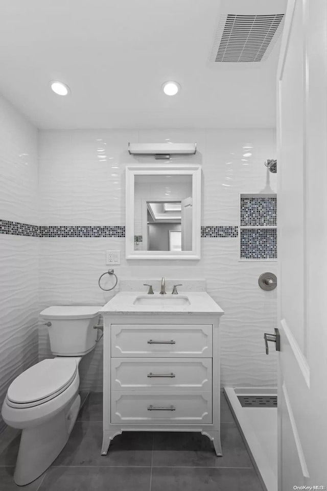 bathroom featuring toilet, a tile shower, tile patterned floors, and tile walls