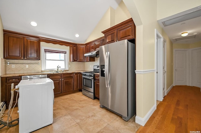 kitchen with vaulted ceiling, appliances with stainless steel finishes, sink, decorative backsplash, and light stone counters