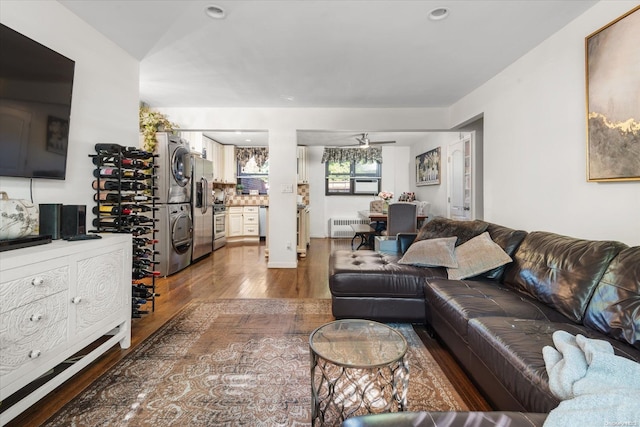 living room with hardwood / wood-style floors, ceiling fan, stacked washer and dryer, and radiator