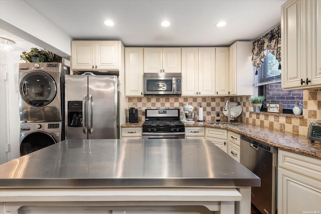 kitchen with cream cabinets, decorative backsplash, stacked washer and dryer, and stainless steel appliances